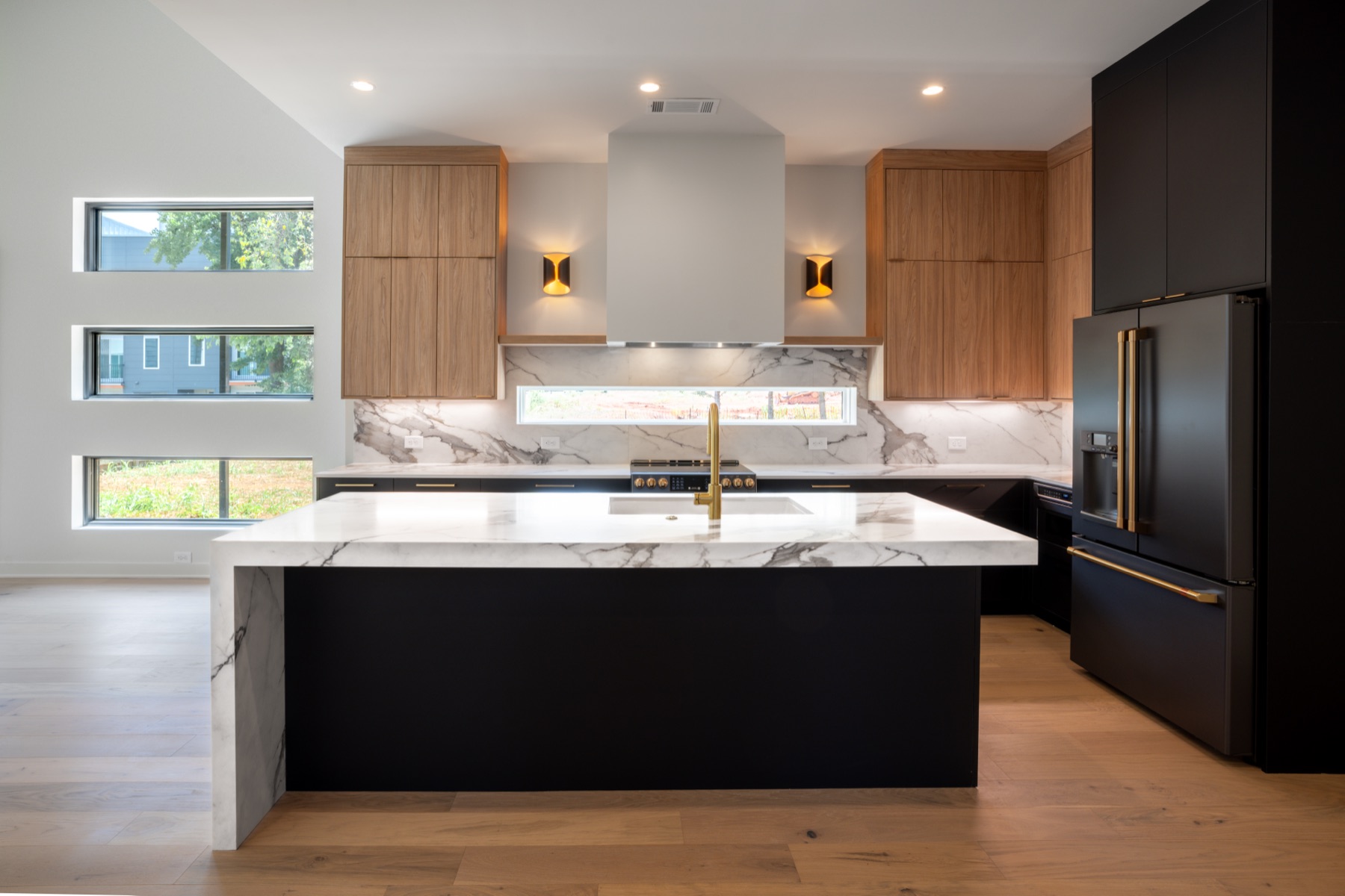 Kitchen with marble waterfall island, black cabinetry and walnut uppers